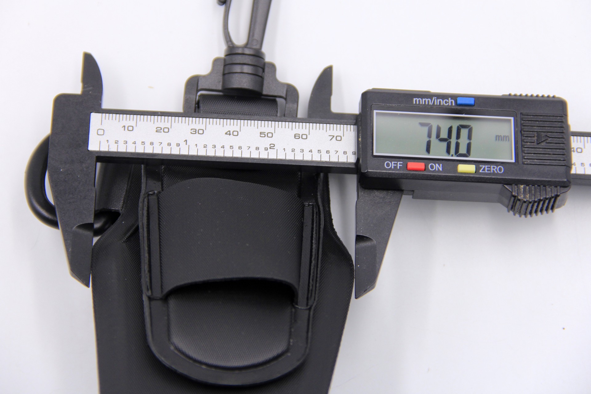 Digital caliper measuring the width of a black WEFOX EVA Plier Pouch at 74.0mm, showing the pouch's front view with its textured EVA construction, belt clip attachment, and elastic securing strap against a white background.