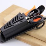 **Alt Text:** Close-up angled view of a WEFOX EVA plier pouch in black with ventilated chevron-pattern cutouts and a belt clip, shown open on a wooden cutting board with a pair of black-and-orange fishing scissors and a lip grip tool stored inside, highlighting the pouch's organized multi-tool storage capacity and durable EVA construction.