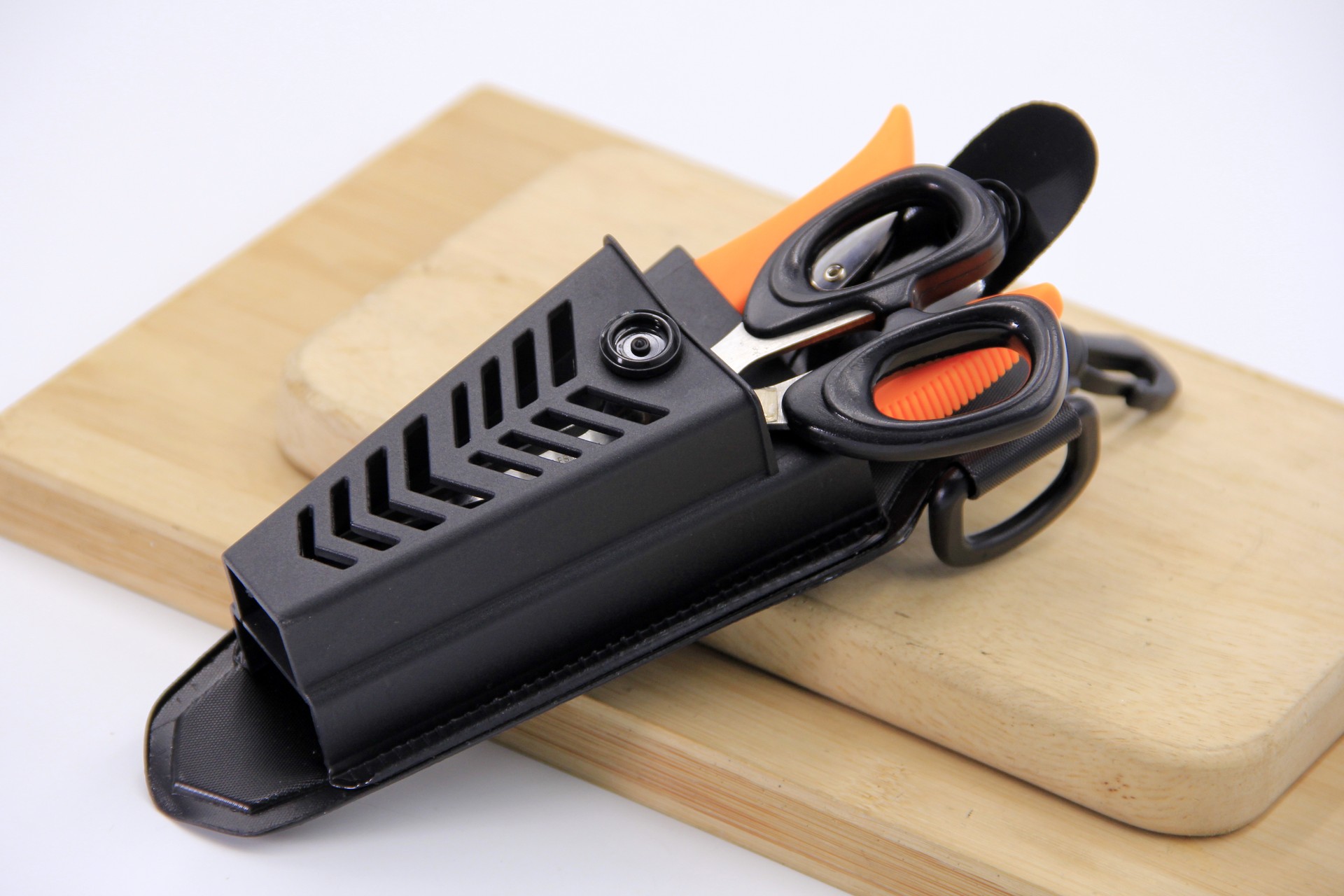 **Alt Text:** Close-up angled view of a WEFOX EVA plier pouch in black with ventilated chevron-pattern cutouts and a belt clip, shown open on a wooden cutting board with a pair of black-and-orange fishing scissors and a lip grip tool stored inside, highlighting the pouch's organized multi-tool storage capacity and durable EVA construction.