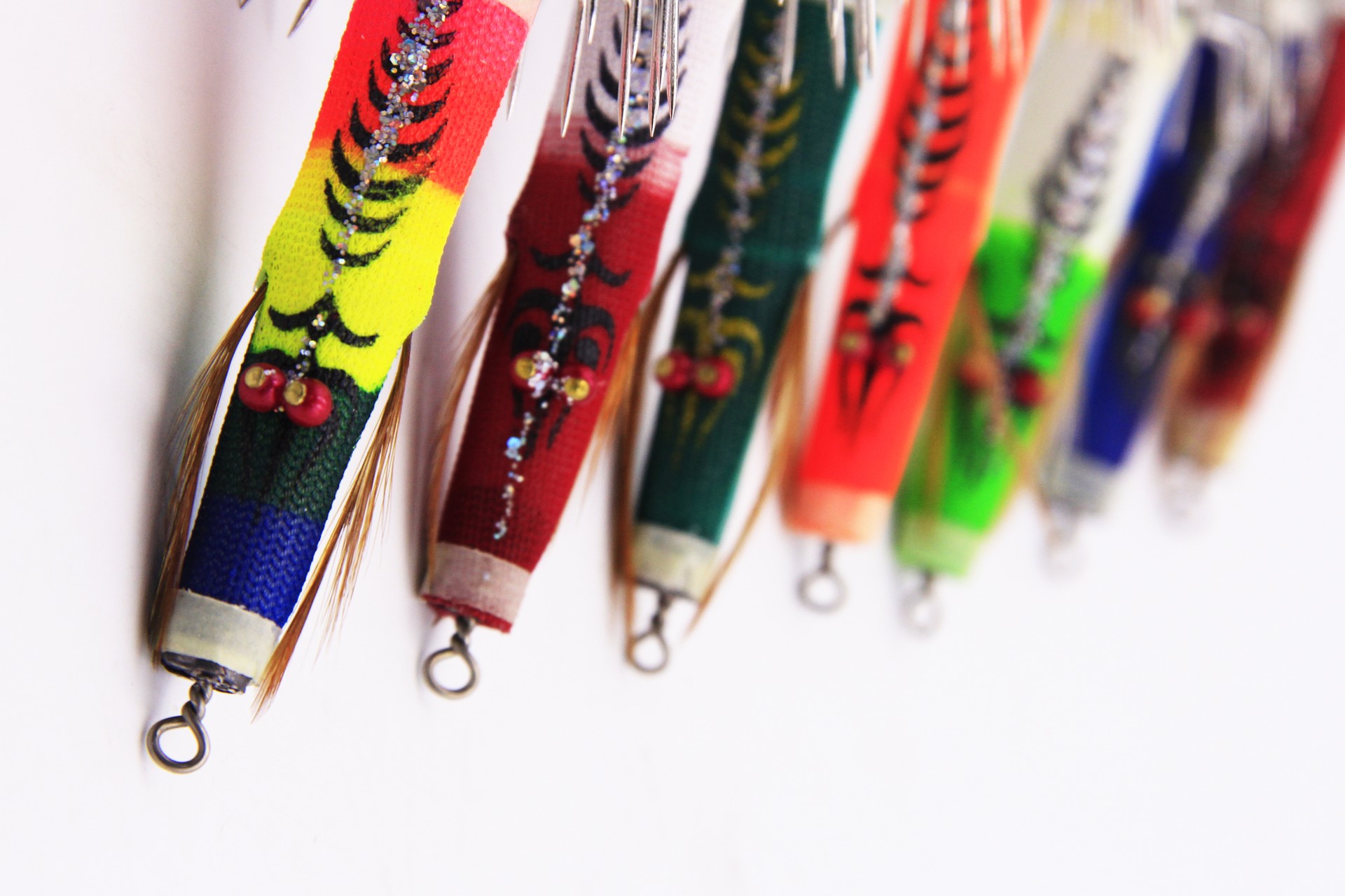 Colorful Bocean Candat Twist Squid Jig Bottom Sinkers hanging in a row on white background, luminous bodies and umbrella hooks in 12 vibrant shades.