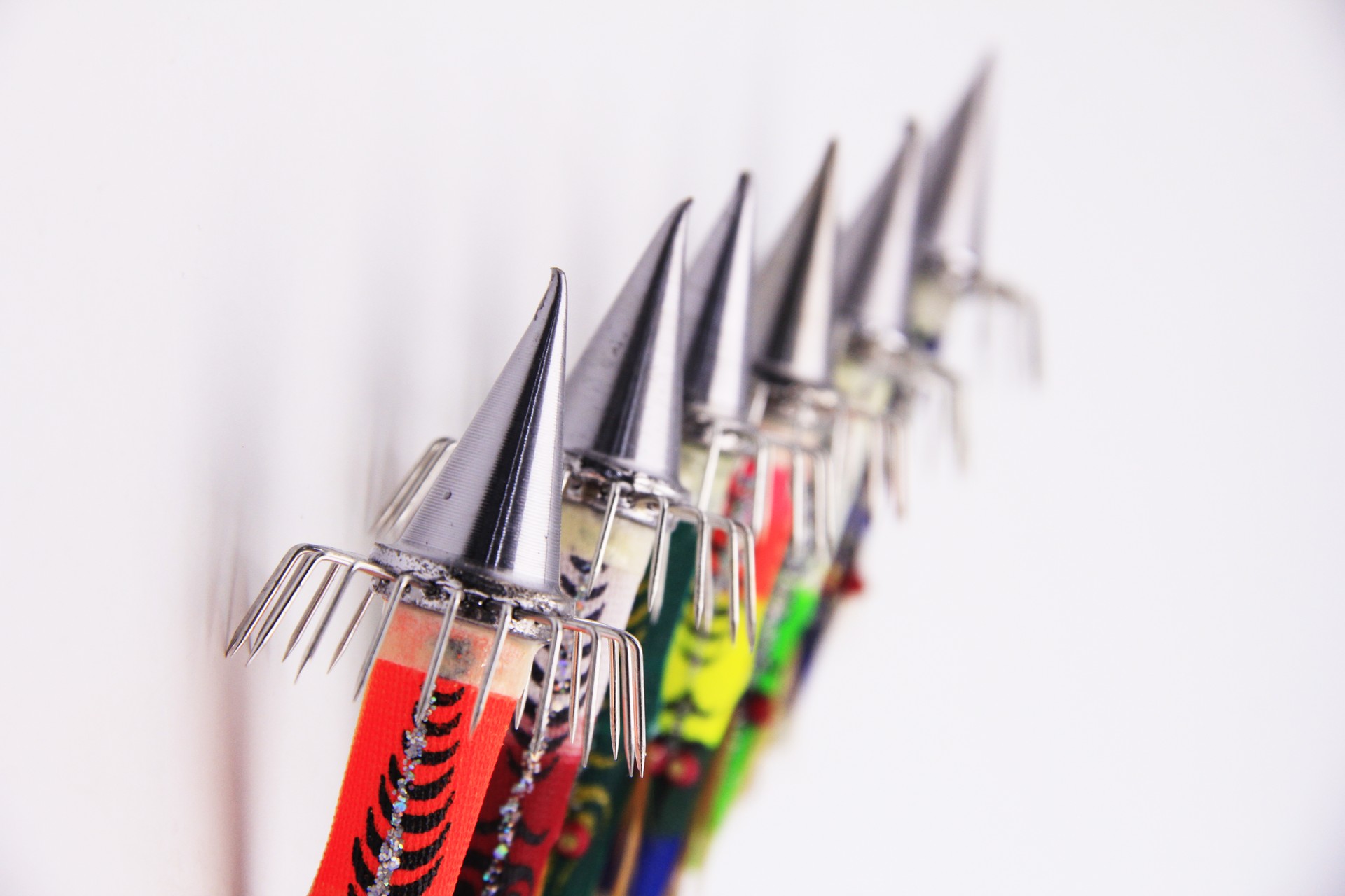 Row of colorful Bocean Candat Twist Squid Jig Bottom Sinkers with luminous cone sinkers and umbrella hooks on white wall.