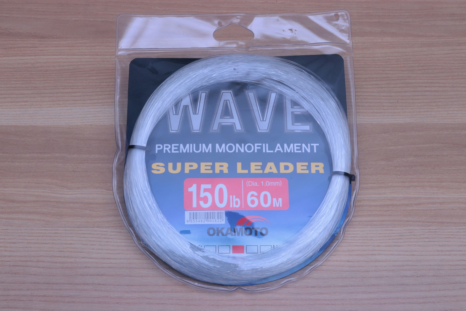 Okamoto Wave Super Soft Leader 150lb premium monofilament leader line in clear packaging on wooden surface.