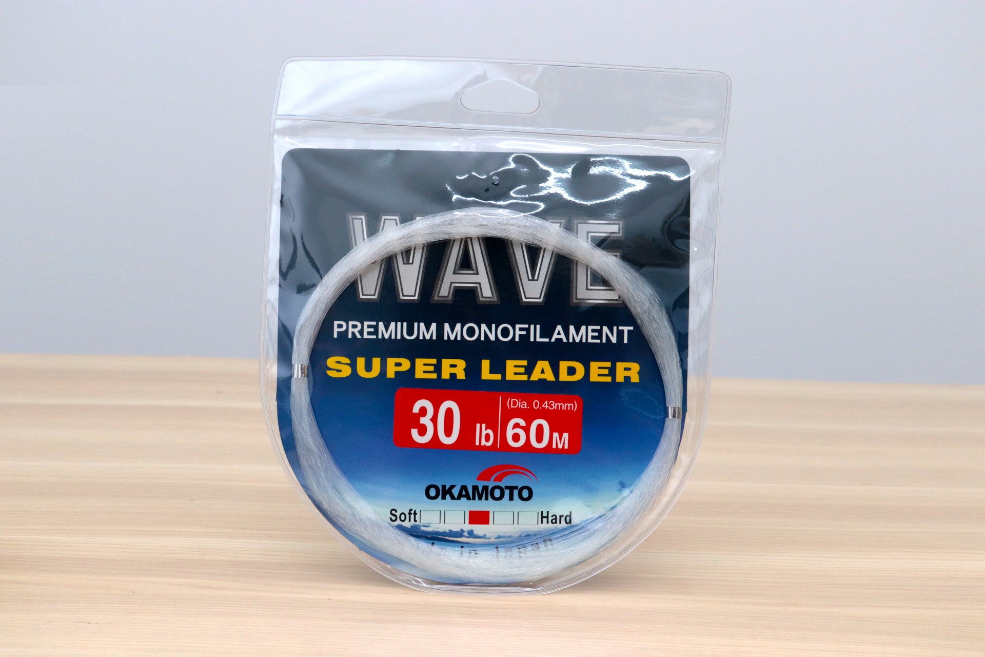 Okamoto Wave Super Soft Leader 30lb 0.60mm 60m premium monofilament leader line in clear hanging package on wood table.