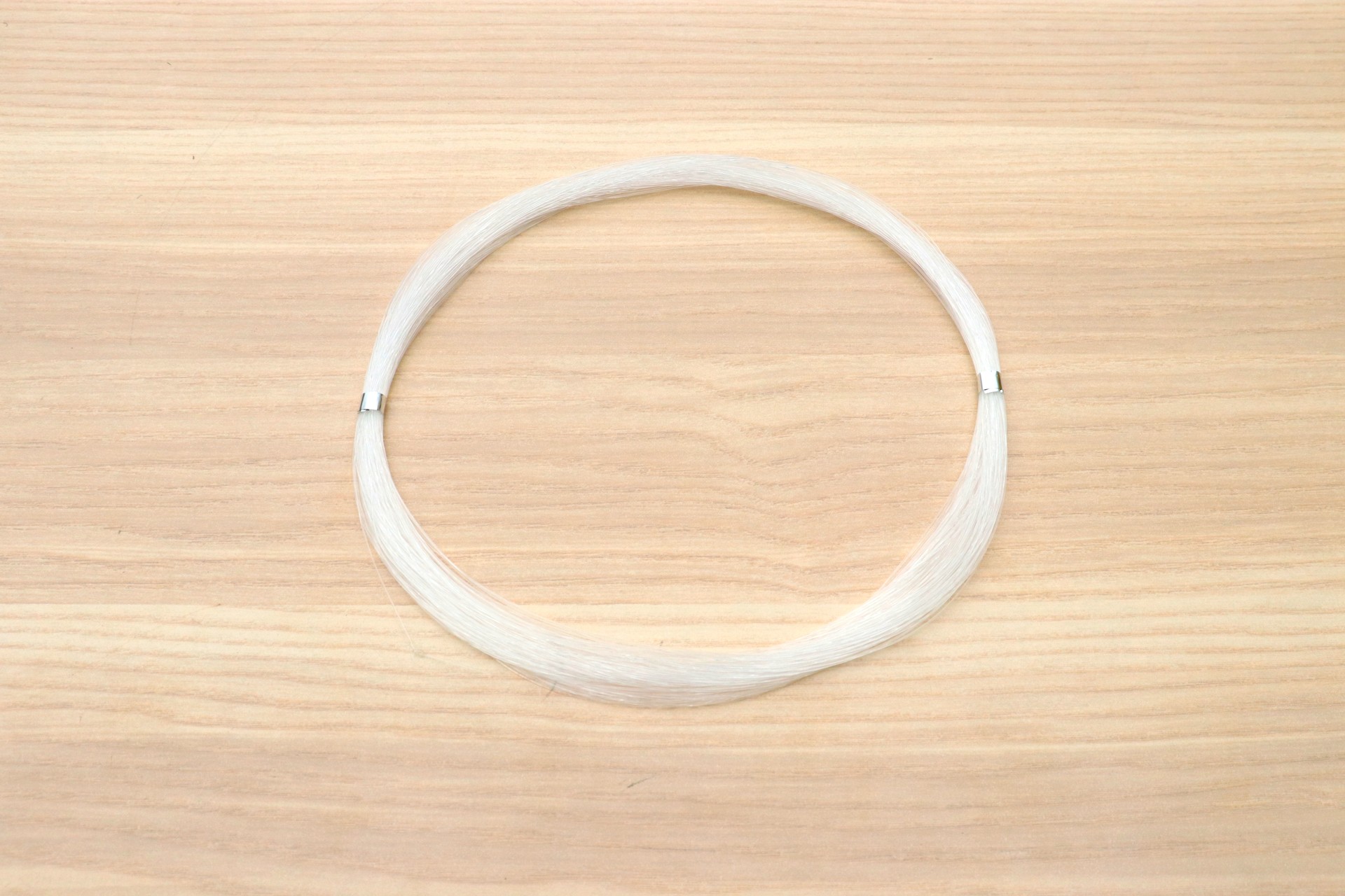 Okamoto Wave Super Soft Leader monofilament laid flat in white circle with metal ends on light wood table, showing ultra-low memory.